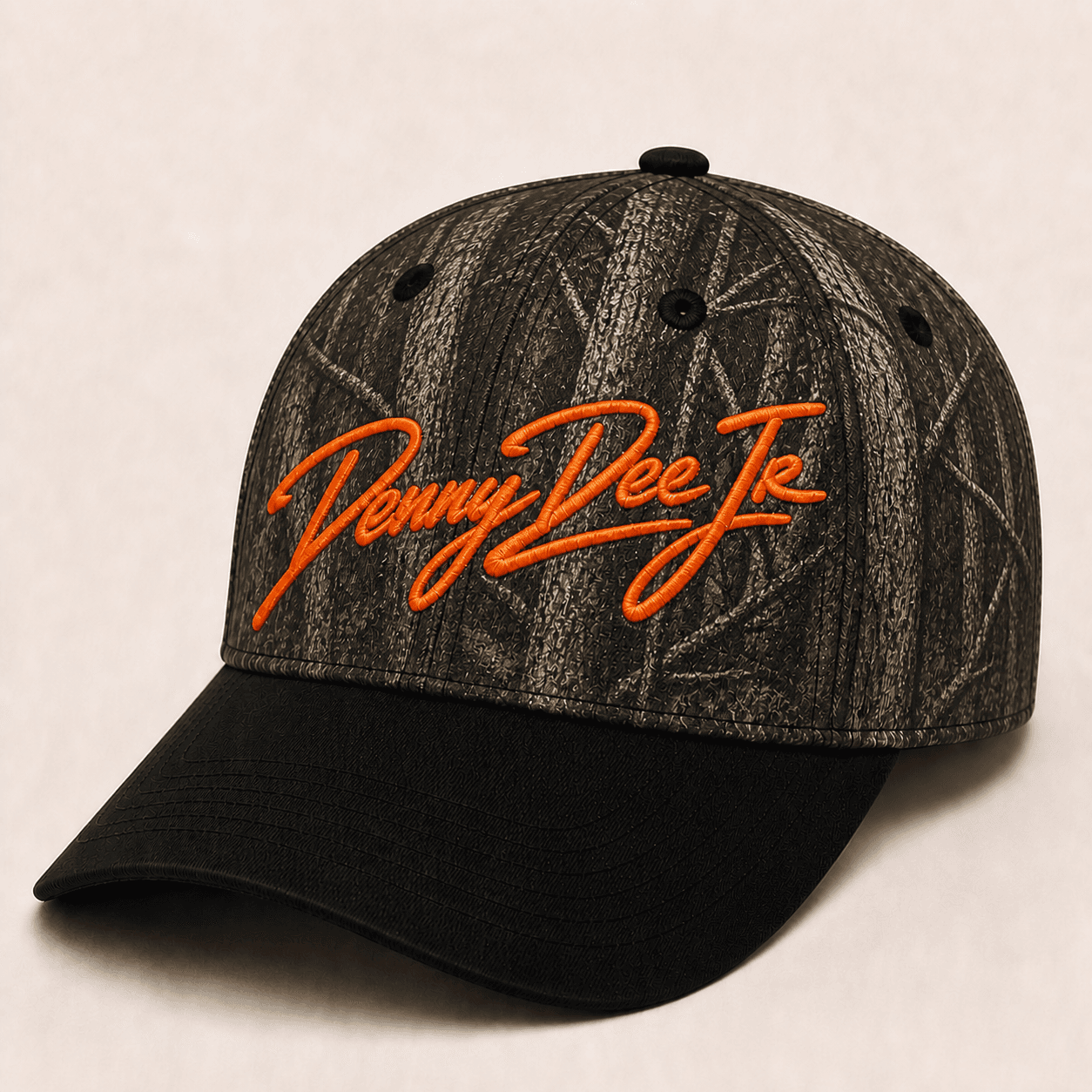 Dark bottomland-inspired bark camo baseball cap with a black brim and blaze-orange embroidered Denny Dee Jr signature